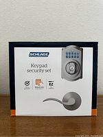 Front view of the box showcasing Schlage keypad deadbolt lock and satin nickel accent lever handle images, highlighting electronic keypad security set features.