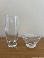 Two clear crystal items: a tall Skruf vase and a scalloped-edge Villeroy & Boch Paloma Picasso bowl, side by side on wood surface.