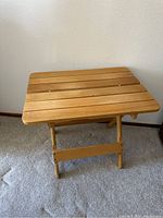Solid wood folding table set up on carpeted floor, showing slatted wood design and foldable legs.