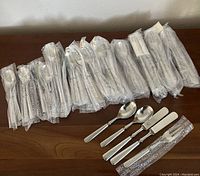 Overview of individually wrapped flatware pieces laid out on wooden surface with sample loose utensils.
