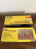 Photo of the closed boxes for the Stanley 18-piece screwdriver set and 5-piece professional pliers set showing packaging and tool images.