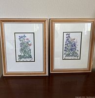 Two vintage wooden framed floral watercolor paintings side by side on a dark wood surface.