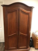 Front view of the closed armoire showing curved doors and metal handles.