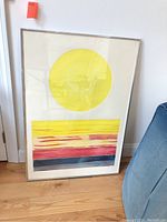 Framed print showing large yellow circle with abstract horizontal stripes in yellow, red, and blue colors.
