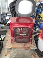 Overall view of red cast iron wood stove on moving dolly in garage setting