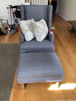 Front view of gray wingback chair with matching ottoman and two patterned pillows.