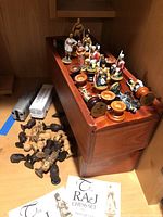 Photo showing British metal figurine chess pieces arranged in a wooden storage box, with some detached wooden African chess pieces to the side and metal figures showing historical soldier designs.