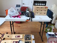 Front view of white folding table showing various items on top including wooden box and other items not included.