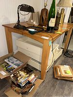 Wooden high table with various items placed on and around it, showing legs and side profile with visible wood grain and drawer units underneath.