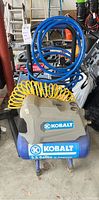 Front view of Kobalt air compressor with attached hoses and surrounding items in garage.