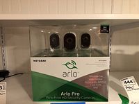 Front view of sealed Arlo Pro security camera kit box showing 3 cameras visible through transparent display window.