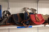 Shelf showing three purses including a black and white polka dot fabric purse, dark brown leather and navy leather flap purses, and a red leather purse with tan straps.