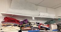 Shelf containing a large roll of white felt or batting with various folded stacks of colorful quilting fabric beneath it