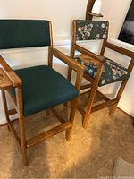 Two wooden billiard chairs shown side by side, one with plain green fabric and one with billiard print upholstery.