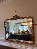 Front view of large antique rectangular gold mirror with ornate top and bottom frame design