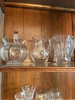 Top shelf with three different clear glass pitchers showing varied shapes and handle designs