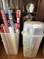 Photo showing several rolls of Christmas-themed wrapping paper including patterns with snowmen, Santa Claus, red and white snowflakes, solid red and white. White translucent tissue paper visible among rolls.