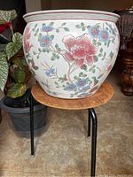Front side view showing large pink and red flowers with blue flowers and green leaves on white ceramic planter.