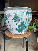 Side view of ceramic planter showing florals, green lily pads, and a bird standing near water painted on the side.