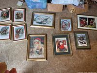 Nine framed Christmas/winter Santa art prints displayed on tiled floor, showing a variety of scenes and frame styles.