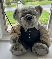 Front view of gray-furred jointed stuffed bear dressed in beige shirt and pinstriped vest holding stick