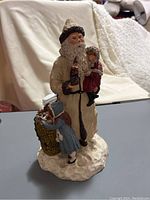 Full view of the Santa Claus figurine holding a child and a young girl leaning on a basket, set on a snow-like base.