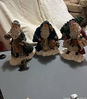 Three Santa figurines displayed side by side on a table, all signed by June McKenna.