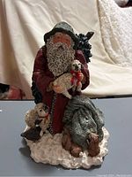 Front and closer view of June McKenna 1991 Santa Claus figurine holding lamb with another lamb at his feet and small animals on snowy base