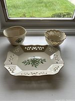 The set displayed on a window sill: the serving tray with holly pattern and cutout edges in the foreground; two bowls behind it showing their different shapes and gold trim.