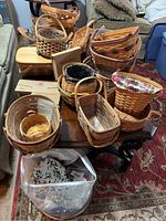 Overview of various woven baskets arranged on a wooden table including Longaberger baskets and boxes with bricks