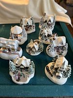 Overview of 9 snow covered miniature Christmas buildings and figures placed on a cloth background