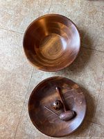 Photo showing two smooth walnut wood bowls with rich wood grain patterns placed on tiled floor.
