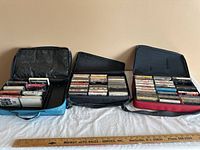 Overview of three soft carrying cases filled with vintage cassette tapes arranged on a white cloth.