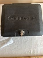 Closed view of the black SentrySafe fire safe showing embossed logo and key lock with key inserted