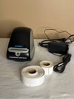 Photo showing Dymo LabelWriter 450 Turbo label printer, power adapter and two rolls of labels on a white surface.