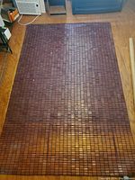 Full view of large dark brown bamboo mat laid on floor showing overall size and condition with some dirt and wear.