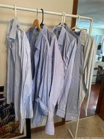 Six men's dress shirts hanging on a clothing rack showing various blue and checked patterns and collars.