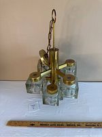 Full view of gold-toned chandelier with 9 clear, textured glass cubes arranged around a central gold metal piece, hanging chain visible.