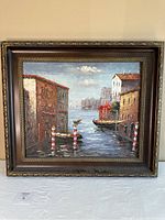 Framed oil painting showing canal, boats, buildings and sky, overall front view