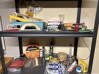 Shelf view showing paint trowels, brushes, boxed spray gun, PVC air hose, wax rings, and other supplies