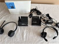 Two complete sets of Plantronics wireless headsets, bases, chargers, cables, and one retail box on a white surface