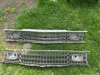 Two front grills laid out on grass, showing full grills with headlight housings and 'PLYMOUTH' lettering