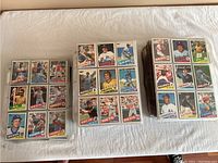 Three stacks of 1985 Topps baseball cards displayed on a flat surface in protective sleeves, showing multiple cards featuring players from teams like Mets, Braves, Reds, Orioles, Dodgers, Cardinals, and more.