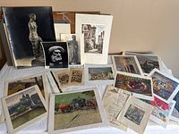 Various art prints laid out on a table showing sculptures, city streets, landscapes, and horse-drawn wagons
