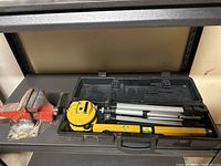 Photo showing the red bench vice, yellow laser level in black carrying case, spirit level on a shelf.
