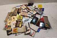 Pile of diverse matchbooks showing many different cover designs and colors spread out on a surface.