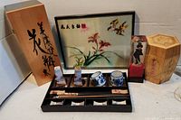 Photo showing the full Asian lot, including chopstick set in a black tray, framed botanical and bird wall art, wooden hexagonal container, and wooden box with Asian script.