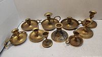 Photo showing all 10 brass candle holders arranged in staggered rows, displaying variety of styles and sizes.