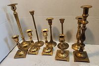 Front view of seven brass candle holders arranged in two rows showing variety of designs and sizes