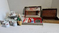 Porcelain tea cup and saucer set, calligraphy brushes and ink accessories in open decorative box, copper box with wooden interior, and small clay figurine.